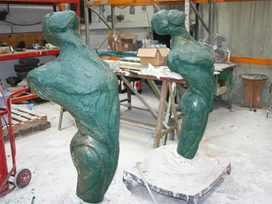 Two unfinished bronze male figures in a workshop.