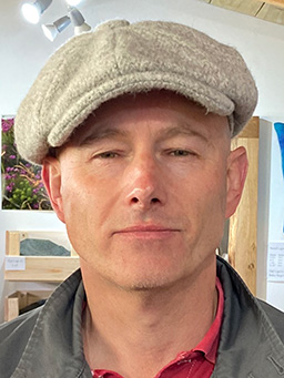 A clean-shaven man wearing a pale-coloured cap.
