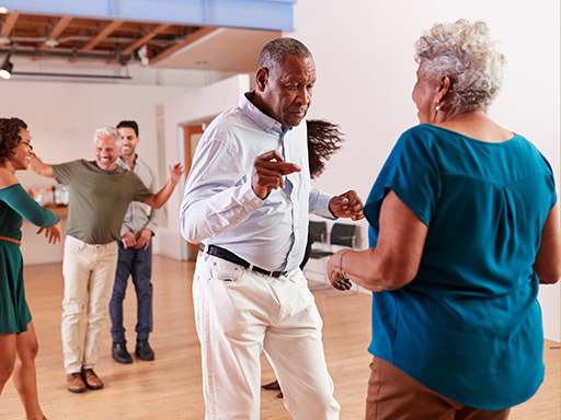 Some younger and older people exercise and dance in a large room.